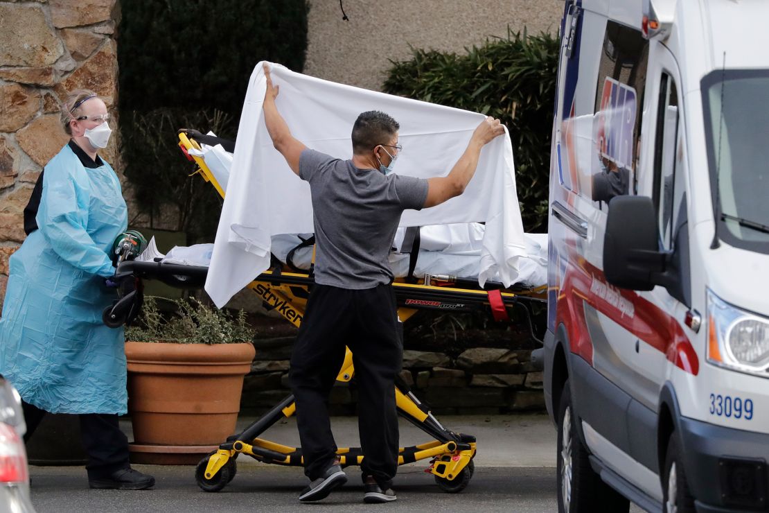 A staff member blocks the view as a person is taken by a stretcher to a waiting ambulance from a nursing facility where dozens of people are being tested for coronavirus.