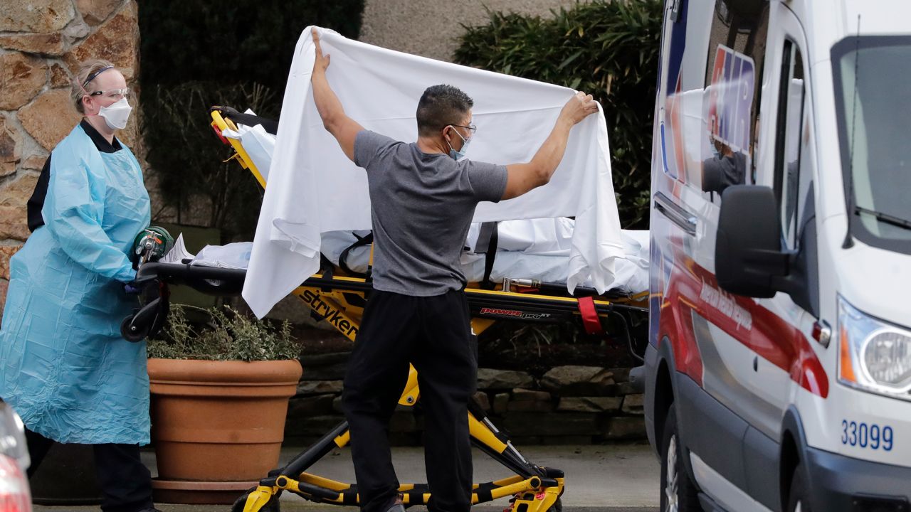A staff member blocks the view as a person is taken by a stretcher to a waiting ambulance from a nursing facility where dozens of people are being tested for coronavirus. 