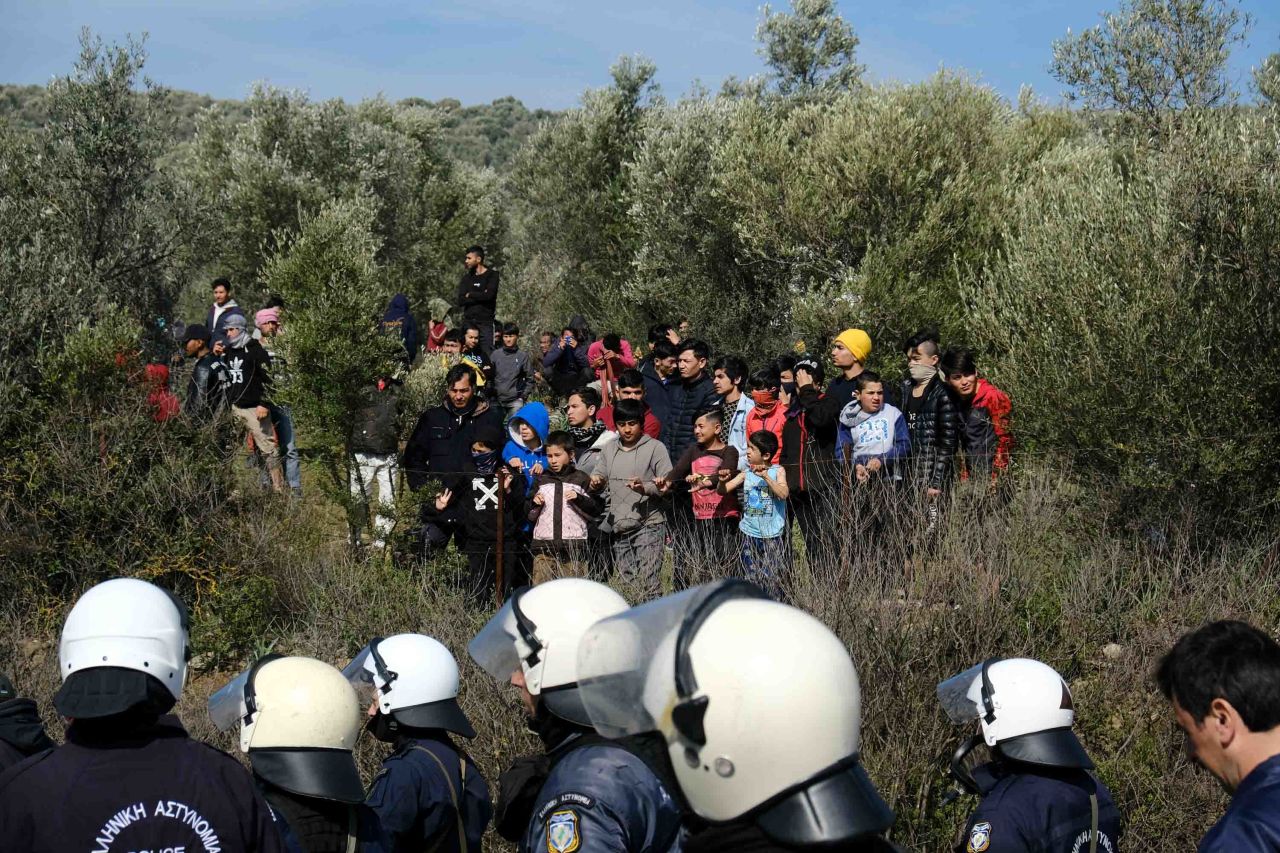 Migrants look on as police block a road near the Moria refugee camp.