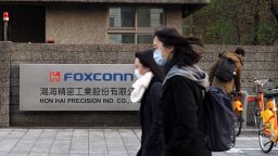 People wearing face masks walk past the logo of Hon Hai Group, also known as Foxconn, in New Taipei City, Taiwan, 18 February 2020.