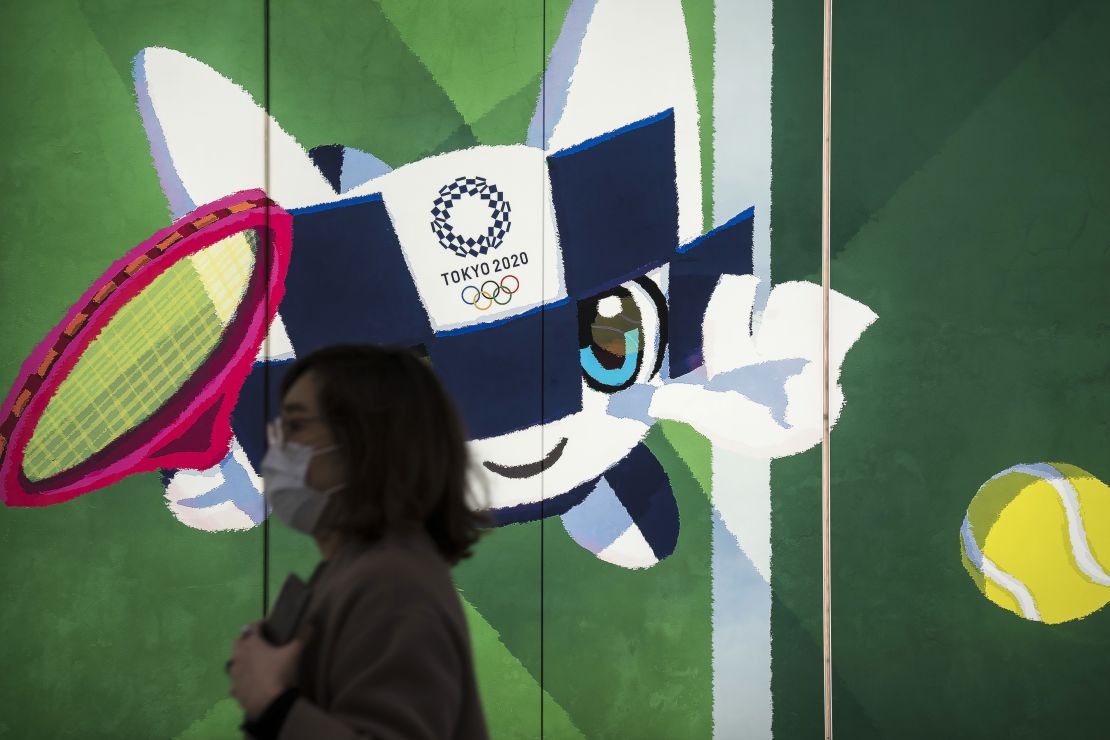 A pedestrian wearing a face mask walks past a display with an illustration of the 2020 Tokyo Olympic and Paralympic Games mascot character Miraitowa on February 26, 2020 in Tokyo, Japan.