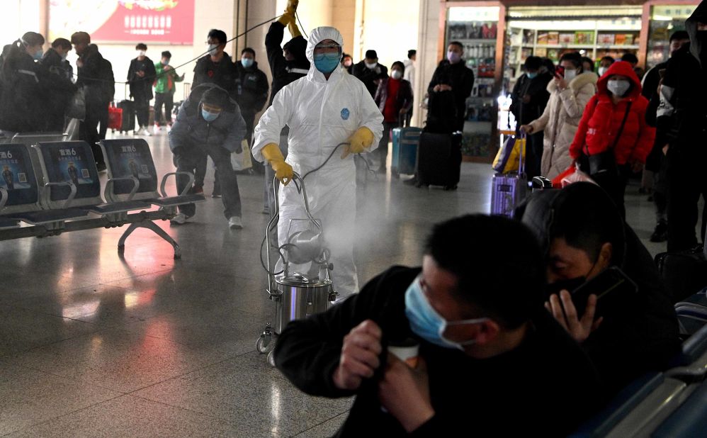 Passengers react as a worker wearing a protective suit disinfects the departure area of a railway station in Hefei, China, on March 4.