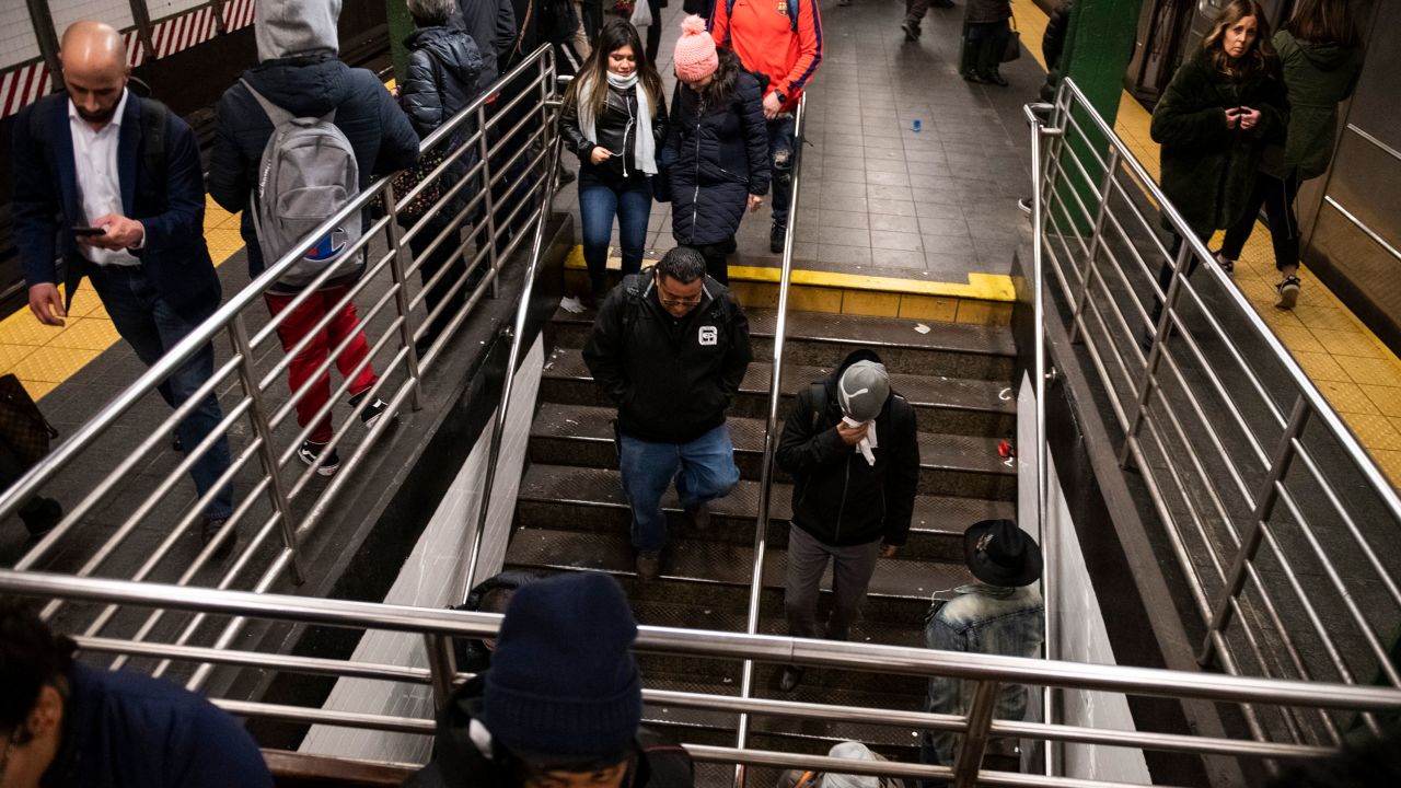 People, including a man covering his mouth and face, walk through the platforms at Times Square in the New York City subway system nearing the start of rush hour in New York, U.S., on Thursday, March 5, 2020. CREDIT: Mark Kauzlarich for CNN