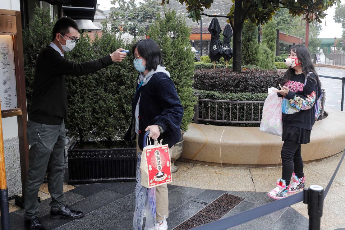 A staff member checks the body temperature of visitors outside Disneytown in Shanghai on Monday.