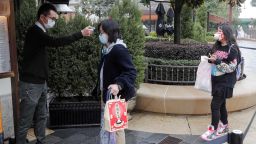 A staff member (L) checks the body temperature of visitors outside Disneytown in Shanghai on March 9, 2020. - China closed most of its makeshift hospitals for coronavirus patients, some schools reopened and Disney resort staff went back to work on March 9 as normality slowly returns to the country after weeks battling the epidemic. Shanghai Disney said it was reopening its shopping and entertainment Disneytown zone -- plus a park and hotel in the same complex -- in the "first step of a phased reopening". The Disneyland amusement park, however, remains closed. (Photo by STR / AFP) / China OUT (Photo by STR/AFP via Getty Images)
