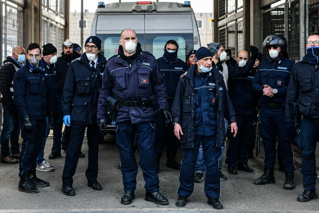 Prison officers stand guard as an ambulance enters SantAnna prison in Modena, inside one of Italy's quarantine red zones, following a disturbance there.
