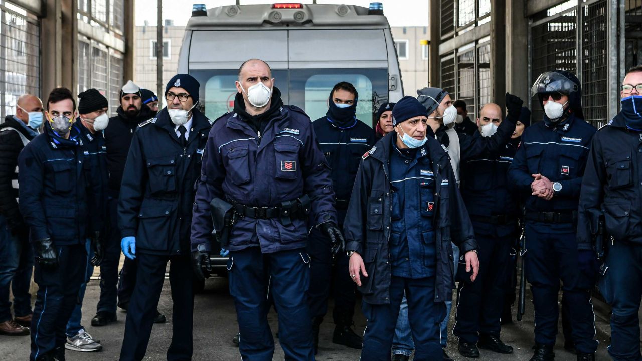 Prison officers stand guard as an ambulance enters SantAnna prison in Modena, inside one of Italy's quarantine red zones, following a disturbance there.