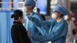 Workers wearing protective clothing (R) check the temperatures of passengers entering the departures area at the Beijing Capital Airport in Beijing on March 5, 2020. - China on March 5 reported 31 more deaths from the new COVID-19 coronavirus epidemic, taking the country's overall toll past 3,000, with the number of new infections slightly increasing. 