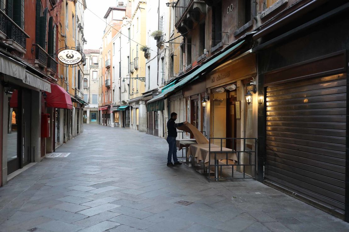 A waiter sets a table in a restaurant on an empty street in Venice, Italy.