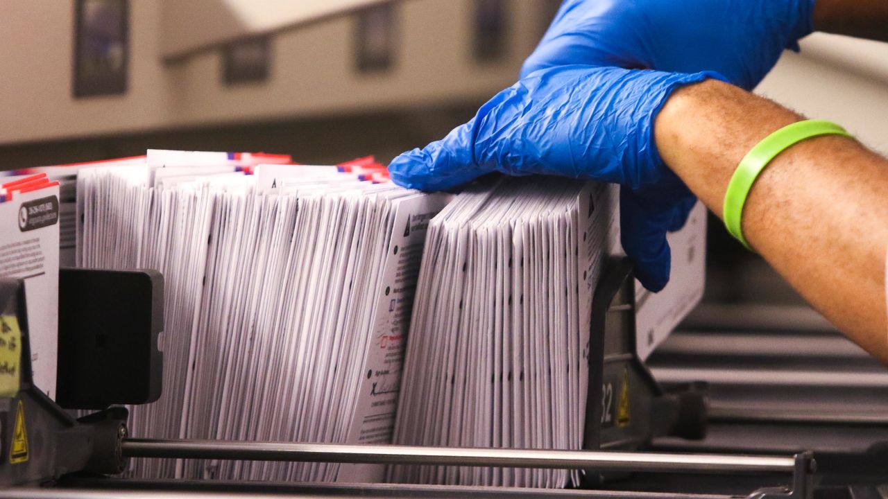 An election worker handles vote-by-mail ballots coming out of a sorting machine for the presidential primary at King County Elections in Renton, Washington on March 10, 2020. 