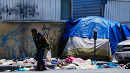 A homeless man walks along a street lined with trash across the street from LAPD Central Community Police Station in downtown Los Angeles on Thursday, May 30, 2019. The union that represents the LAPD is demanding a cleanup of homeless encampments in the city after one detective who works downtown was diagnosed with typhoid fever and two others are showing similar symptoms. (AP Photo/Richard Vogel)