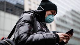 Pedestrian uses her phone while wearing a face mask in Herald Square, Thursday, March 12, 2020, in New York. New York City Mayor Bill de Blasio said Thursday he will announce new restrictions on gatherings to halt the spread of the new coronavirus in the coming days, but he hopes to avoid closing all public events such as Broadway shows. For most people, the new coronavirus causes only mild or moderate symptoms. For some it can cause more severe illness. (AP Photo/John Minchillo)