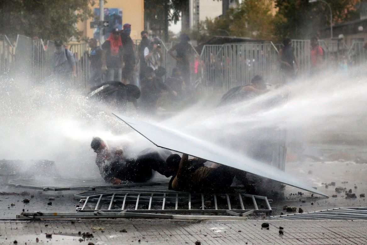 Anti-government protesters are hit by a police water cannon in Santiago, Chile, on Wednesday, March 11.