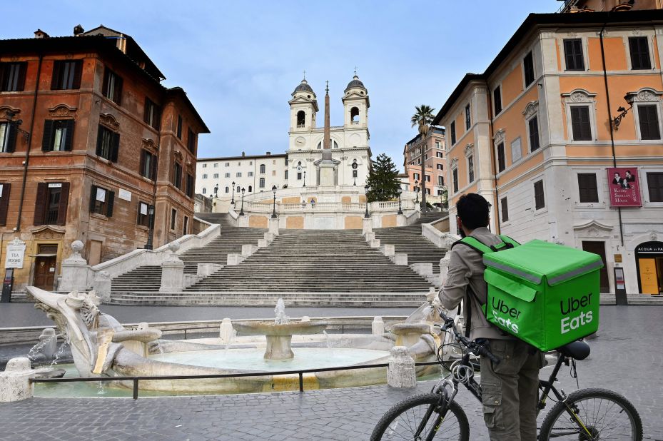 An Uber Eats delivery biker stands at a deserted Piazza di Spagna in Rome.