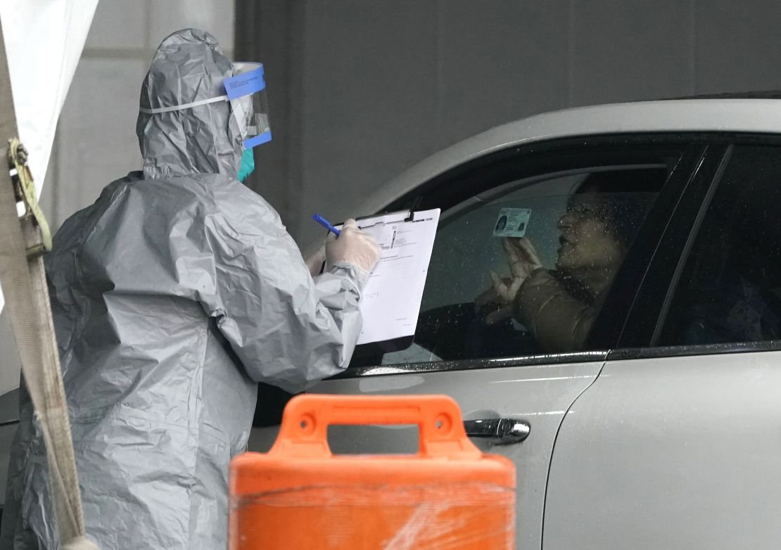 Workers in protective suits check IDs as people arrive to be tested for coronavirus at a drive-up testing facility in Glen Island Park in New Rochelle, New York, on March 13, 2020.