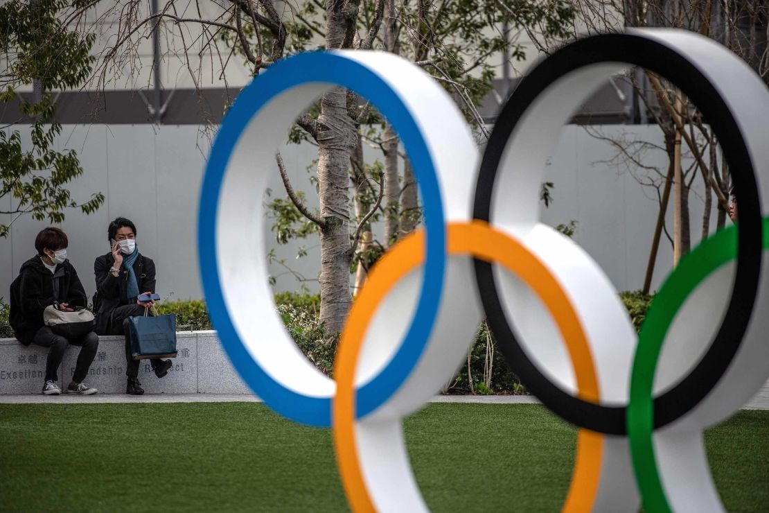 People wearing face masks chat next to the Olympic Rings on March 13, 2020 in Tokyo, Japan. 