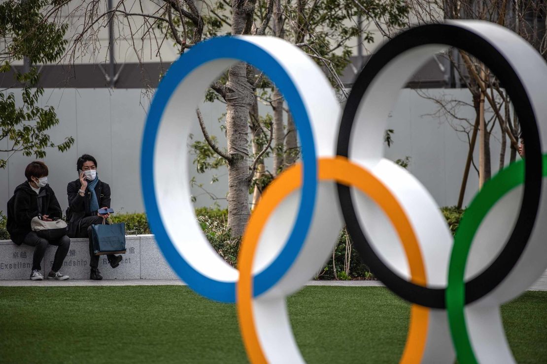 People wearing face masks chat next to the Olympic Rings on March 13, 2020 in Tokyo, Japan.