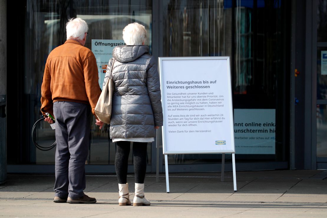 A couple stands in front of a sign that says a store is closed in Germany.