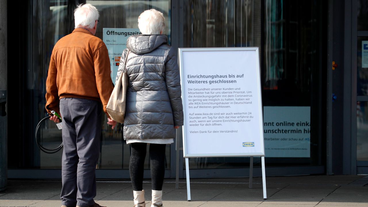 A couple stands in front of a sign that says a store is closed in Germany.