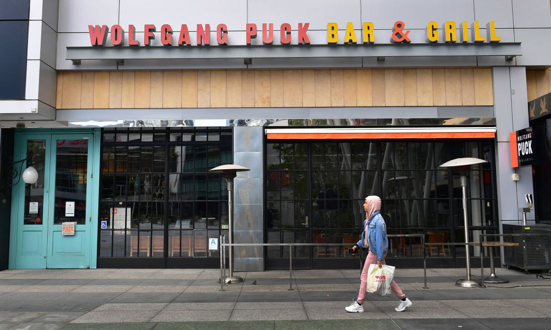 A pedestrian walks past a closed 'Wolfgang Puck Bar & Grill' restaurant  in Los Angeles, California on March 17, 2020 as the coronavirus epidemic leads to restaurant and school closures as workers work from home in an effort to encourage social distancing. - The White House has suggested gatherings limited to 10 people or less as the number of coronavirus cases across the country passes 5,000 with 100 dead. (Photo by Frederic J. Brown/AFP/Getty Images)