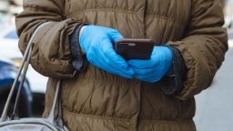 A person wears protective gloves while using a mobile phone in New Rochelle, New York, U.S., on Monday, March 16, 2020. The governors of New York, New Jersey and Connecticut banned all gatherings of 50 or more people, and said bars, restaurants, casinos and gyms must close Monday at 8 p.m. Photographer: Angus Mordant/Bloomberg via Getty Images