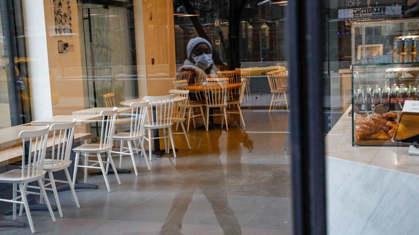 A pedestrian wearing a protective face mask walks past a nearly empty restaurant near Grand Central Terminal, Monday, March 16, 2020, in New York. New York leaders took a series of unprecedented steps Sunday to slow the spread of the coronavirus, including canceling schools and extinguishing most nightlife in New York City. (AP Photo/John Minchillo)