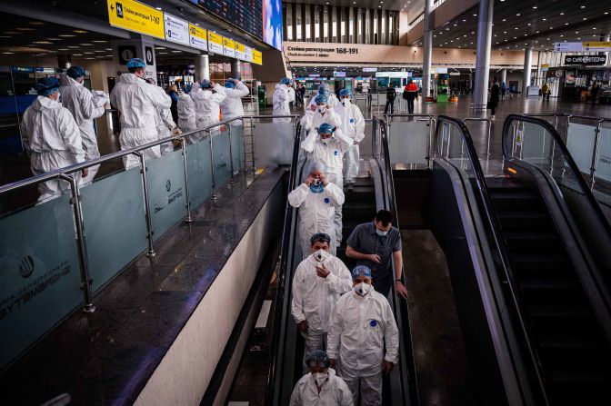 Medical staff wearing protective suits ride down an escalator at Moscow's Sheremetyevo International Airport on March 18, 2020.