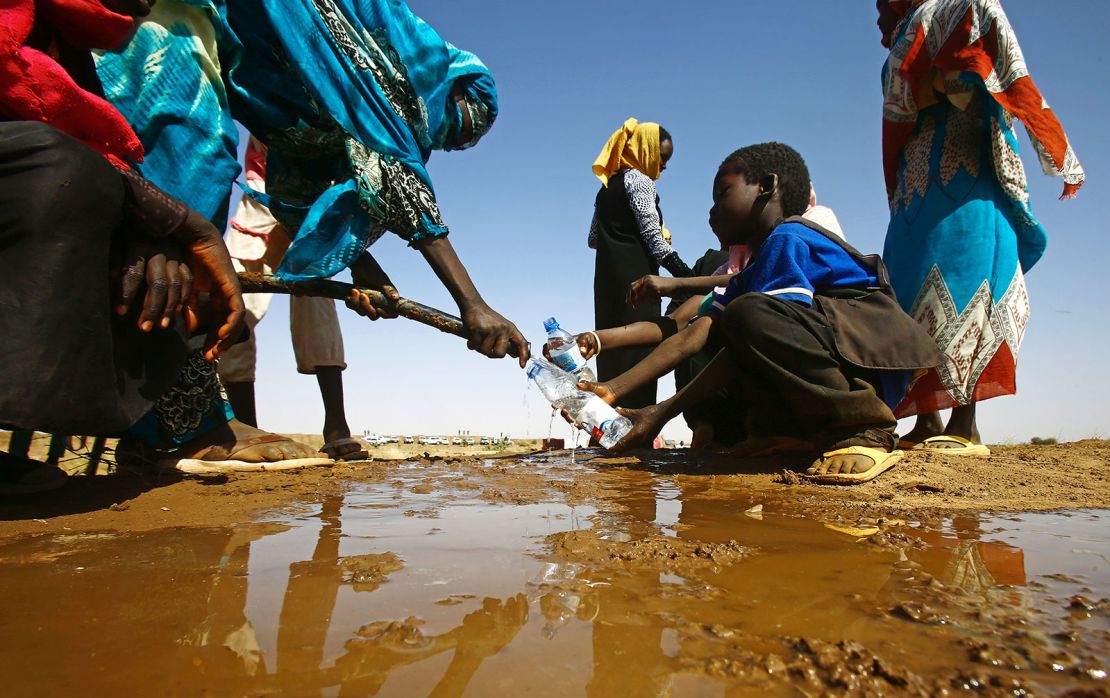  A Sudanese woman fills water bottles held by a young boy near the capital of the North Darfur State. 