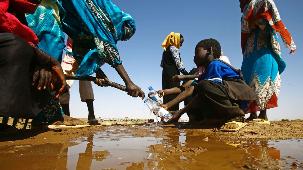 A Sudanese woman fills water bottles held by a young boy near the capital of the North Darfur State.