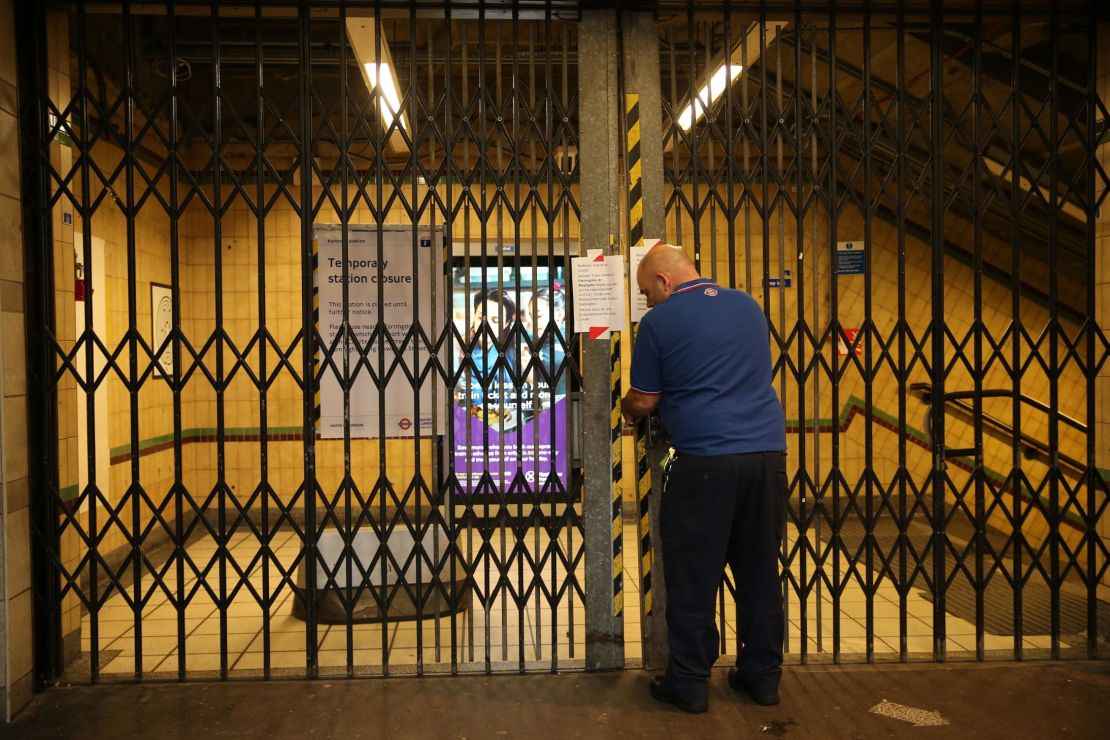 A worker closes the gates at Barbican Underground station as public transport services in London are reduced.