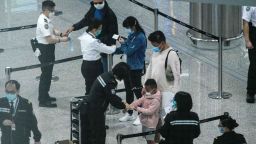 A photo taken through thick glass shows passengers (C) wearing face masks as a precautionary measure against the COVID-19 coronavirus as they receive quarantine tracking wrist bands at Hong Kongs international airport on March 19, 2020. - On March 18, Hong Kong authorities began ordering all arrivals from overseas to wear electronic bracelets, connected to an app to mark your location, and two weeks self-quarantine. 