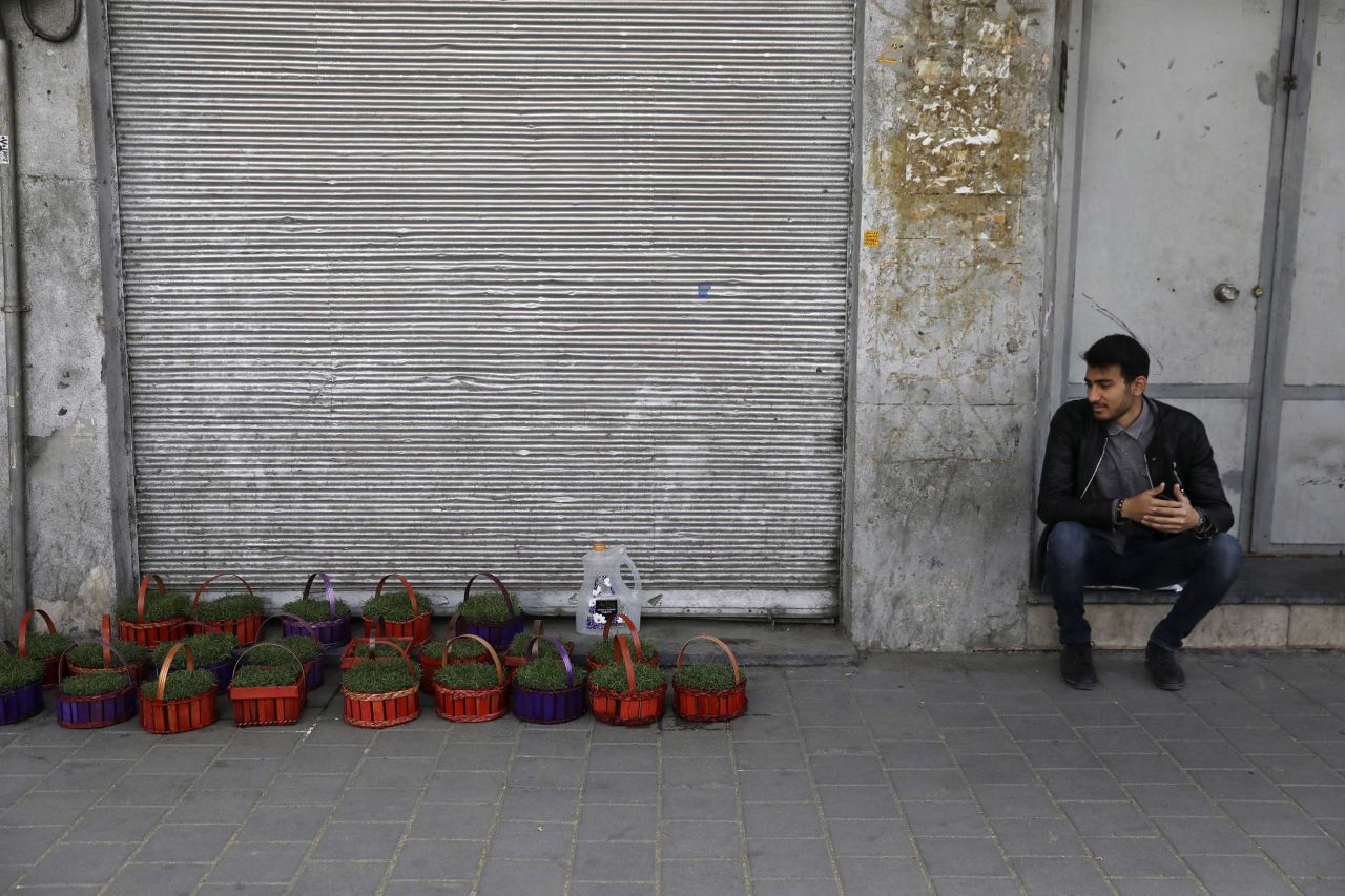 As coronavirus ravages businesses in Iran, a vendor sits next to his baskets of grass shoots ahead of Nowruz in front of closed shops at Tehran's Grand Bazaar. 