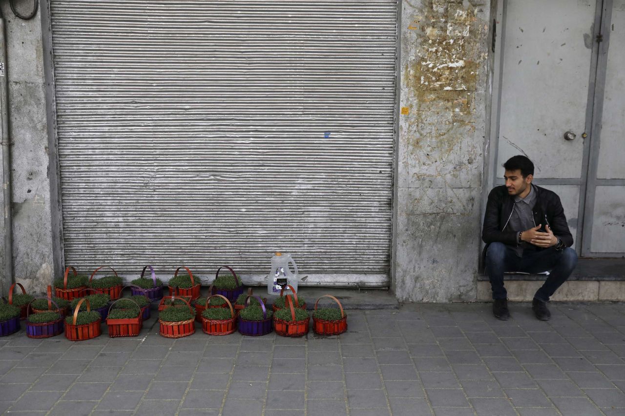 As coronavirus ravages businesses in Iran, a vendor sits next to his baskets of grass shoots ahead of Nowruz in front of closed shops at Tehran's Grand Bazaar.