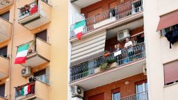 People stand on the balcony as radio stations across the country play the Italian national anthem to raise spirits.