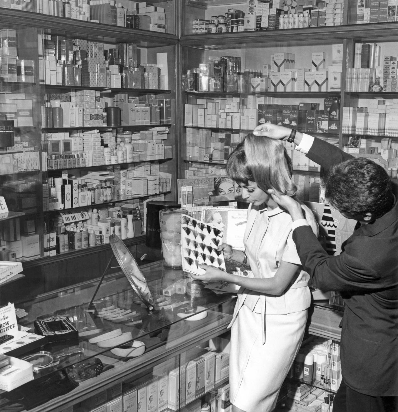 A shop assistant holds a color sample against  a customer's hair in 1965.
