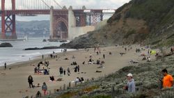 People line Baker Beach near the Golden Gate Bridge on Sunday, March 22, 2020, in San Francisco. Some 40 million Californians are coping with their first weekend under a statewide order requiring them to stay at home to help curb the spread of the coronavirus.