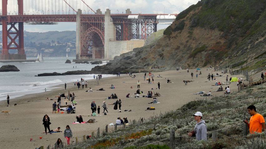 People line Baker Beach near the Golden Gate Bridge on Sunday, March 22, 2020, in San Francisco. Some 40 million Californians are coping with their first weekend under a statewide order requiring them to stay at home to help curb the spread of the coronavirus.