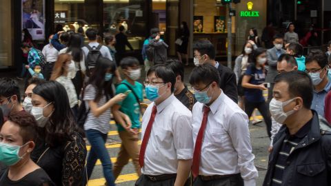 Office workers and pedestrians wearing protective masks walk along Queen's Road Central in the Central district of Hong Kong on Friday, March 20, 2020.