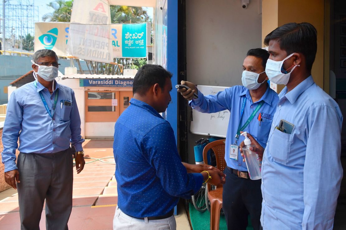 Security personnel wear face masks as they check the temperature of visitors to a hospital in Bangalore on March 16, 2020.