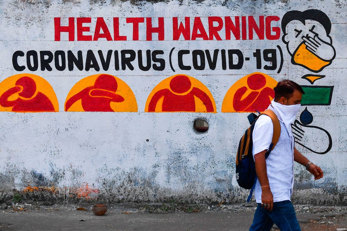 A pedestrian using a handkerchief as a facemask walks past graffiti raising awareness about the pandemic, in Mumbai, on March 23, 2020.