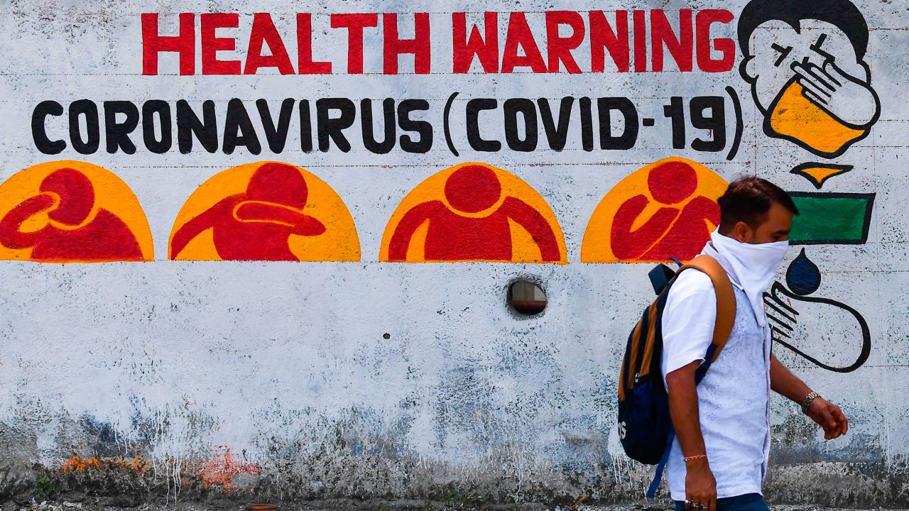 A pedestrian using a handkerchief as a facemask walks past graffiti raising awareness about the pandemic, in Mumbai, on March 23, 2020.
