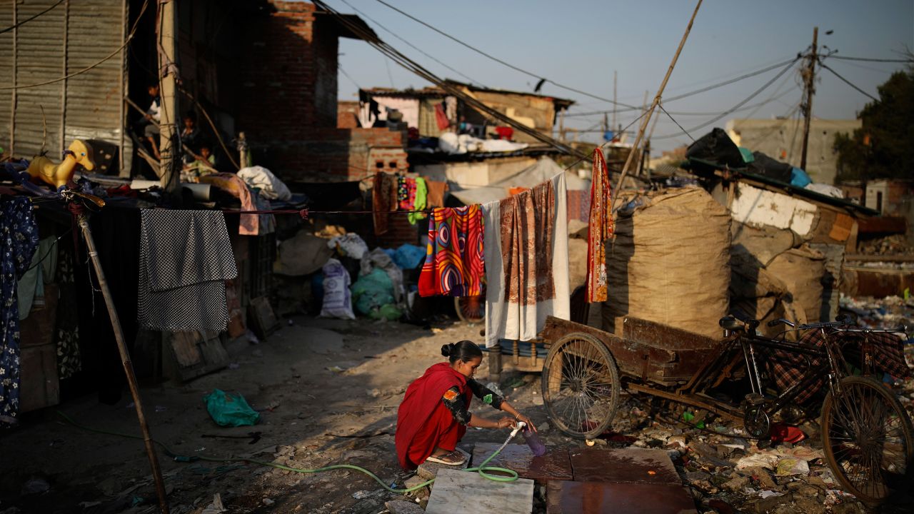 In this Tuesday, March 17, 2020 photo, a woman fills a plastic bottle next to a drain filled with plastic and other filth at a slum in New Delhi, India.