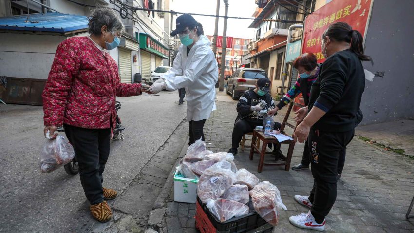 In this March 18, 2020 photo, people buy pork at the entrance gate of a closed residential community in Wuhan in central China's Hubei Province. Last month, Wuhan was overwhelmed with thousands of new cases of coronavirus each day. But in a dramatic development that underscores just how much the outbreak has pivoted toward Europe and the United States, Chinese authorities said Thursday that the city and its surrounding province had no new cases to report. The virus causes only mild or moderate symptoms, such as fever and cough, for most people, but severe illness is more likely in the elderly and people with existing health problems. (Chinatopix via AP)