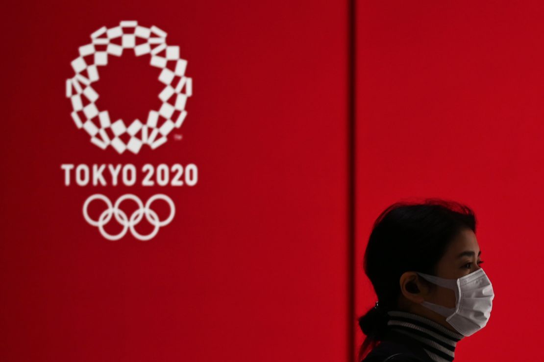 A woman in a face mask walks past a display showing the Tokyo 2020 Olympic Games logo in Tokyo on March 24, 2020.