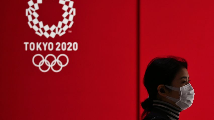 TOPSHOT - A woman in a face mask walks past a display showing the Tokyo 2020 Olympic Games logo in Tokyo on March 24, 2020. (Photo by Charly Triballeau/AFP/Getty Images)