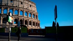 A woman wearing a protective mask waits at a bus stop near the Colosseum monument along a deserted Via dei Fori Imperiali on March 23, 2020 in Rome, during the country's lockdown aimed at stopping the spread of the COVID-19 (new coronavirus) pandemic. (Photo by Filippo MONTEFORTE / AFP) (Photo by FILIPPO MONTEFORTE/AFP via Getty Images)