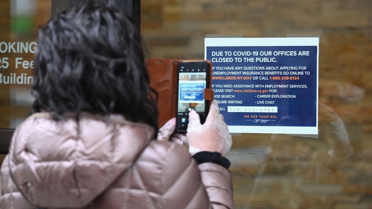 A woman takes a picture of a sign in front of the closed Department of Labor on March 25, 2020 in New York. - Wall Street stocks jumped early Wednesday as markets awaited a vote on a $2 trillion package agreed by congressional leaders to boost the US economy ravaged by the coronavirus outbreak. (Photo by Angela Weiss/AFP/Getty Images)