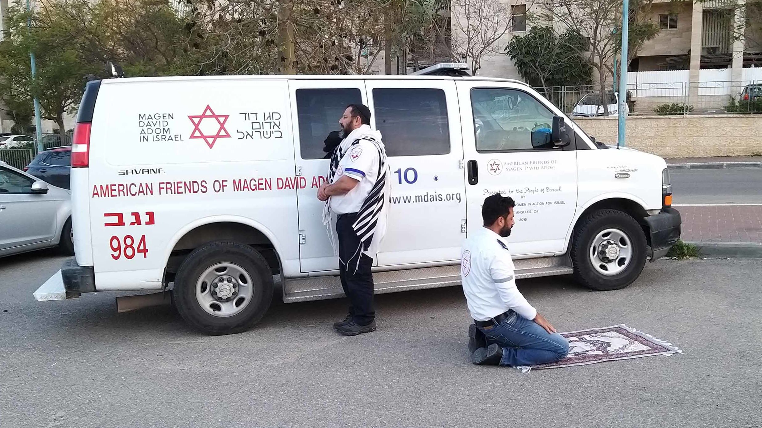 Jewish paramedic Avraham Mintz faces Jerusalem, his prayer shawl hanging off his shoulders. Muslim paramedic Zoher Abu Jama kneels facing Mecca, his prayer rug unfurled before him. 