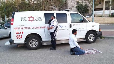 Jewish paramedic Avraham Mintz faces Jerusalem, his prayer shawl hanging off his shoulders. Muslim paramedic Zoher Abu Jama kneels facing Mecca, his prayer rug unfurled before him. 