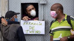 A man wearing a protective face mask as a preventive measure against the spread of the new coronavirus attends customers through an opening from which hangs a handwritten sign that reads in Spanish: "Pharmacy on duty," in Caracas, Venezuela, Tuesday, March 24, 2020. President Nicolas Maduro has ordered the entire nation to stay home under a quarantine aimed at cutting off the spread of the new virus, calling it a "drastic and necessary measure." (AP Photo/Ariana Cubillos)